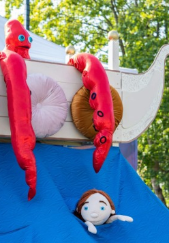 Zdjęcia maskotki ze spektaklu. Imitacja dziecka w wodzie, a obok na białej łodzi kraken.