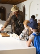 Zdjęcie detektywa w kapeluszu, a obok niego grupka dzieci - uczestników warsztatów.