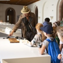 Zdjęcie detektywa w kapeluszu, a obok niego grupka dzieci - uczestników warsztatów.