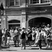 Czarno-białe zdjęcie wielu osób z widokiem Galerii w Bramie w tle.