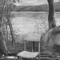 Czarno-biała fotografia przedstawia krzesło stojące na ziemi porośniętej trawą