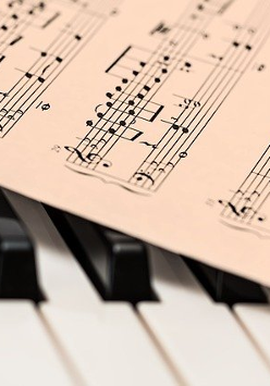 Zdjęcie zeszytu z nutami a pod nim klawisze fortepianu.