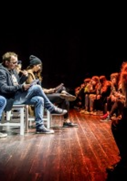 Na zdjęciu fragment przedstawienia. Na scenie, twarzami do widzów, na krzesłach siedzą aktorzy, czytają.