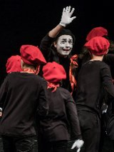 grupa dzieci w czarnych koszulkach i czerwonych beretach wraz z aktorem z umalowana na biało twarzą