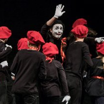 grupa dzieci w czarnych koszulkach i czerwonych beretach wraz z aktorem z umalowana na biało twarzą