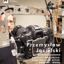W centralnej części zdjęcia widać maszynę fotografującą. W tle stoi mężczyzna w okularach i wpatruje się w obiektyw. W prawym dolnym rogu widnieje tytuł wystawy i nazwisko autora.