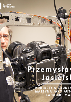 W centralnej części zdjęcia widać maszynę fotografującą. W tle stoi mężczyzna w okularach i wpatruje się w obiektyw. W prawym dolnym rogu widnieje tytuł wystawy i nazwisko autora.