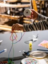 ręce dziecka trzymającego szpule z wstązką na stołem z innymi materiałami plastycznymi