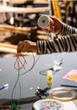 ręce dziecka trzymającego szpule z wstązką na stołem z innymi materiałami plastycznymi