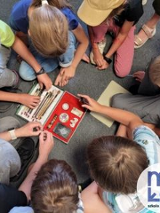 zdjecie z góry na którym widać dzieci siedzące na podłodze, wyciągają przybory z otwartego pudełka