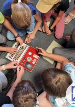 zdjecie z góry na którym widać dzieci siedzące na podłodze, wyciągają przybory z otwartego pudełka