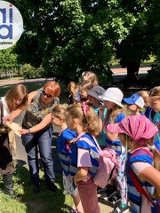 dzieci przypatrujące sie przedmiotowi trzymanemu przyz opiekuna w plenerze