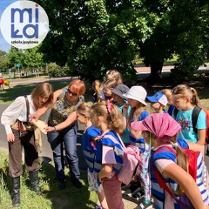 dzieci przypatrujące sie przedmiotowi trzymanemu przyz opiekuna w plenerze