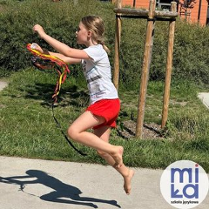 dziewczynka, która wykonuje skok z kolorowymi wstążkami w ręku w plenerze