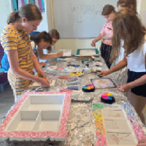 Zdjęcie przedstawia grupę dzieci, która zebrana wokół stołu wykonuje rękodzieło.