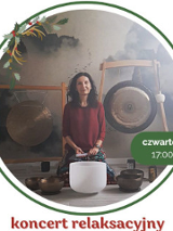 Zdjęcie przedstawia kobietę siedzącą przed dużym gongiem oraz kilkoma misami do śpiewu. Kobieta ma na sobie czerwoną koszulkę, ciemne włosy i patrzy w obiektyw aparatu. Kobieta lekko się uśmiecha.