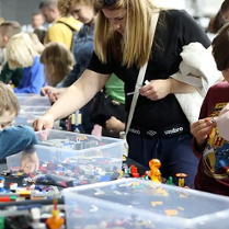 Dzieci siedzą przy stołach i układają klocki Lego.