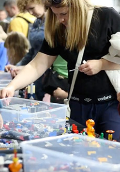 Dzieci siedzą przy stołach i układają klocki Lego.