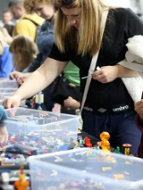 Dzieci siedzą przy stołach i układają klocki Lego.