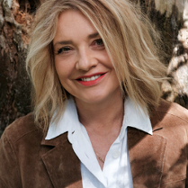 na zdjęciu uśmiechnięta kobieta z włosami do ramion, w białej bluzce i jasnej kurtce