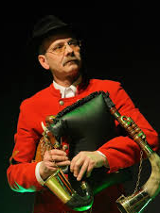 Na zdjęciu dudziarz w czerwonym ubraniu trzymający instrument muzyczny.