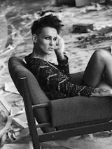 Artystyka siedzi w szpilkach i skuience na krześle, dookoła bałagan "remontowy". Zdjęcie czarno-białe.