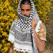 Grafika na tle miętowego koloru. Na środku znajduje się zdjęcie mężczyzny z brodą i długimi ciemnymi włosami, ubranego w kefiję.