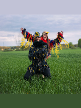 Kobieta i mężczyzna przebrani za kolorowe ptaki pozują do zdęcia. Stoją na zielonej polanie.