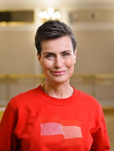 Zdjęcie uśmiechniętej Danuty Stenki w czerwonym swetrze. Jasne tło.