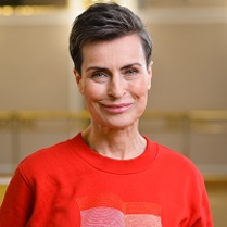 Zdjęcie uśmiechniętej Danuty Stenki w czerwonym swetrze. Jasne tło.