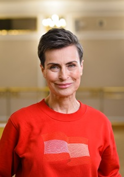 Zdjęcie uśmiechniętej Danuty Stenki w czerwonym swetrze. Jasne tło.