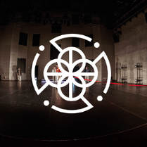 Zdjęcie sceny i czterech stojących na niej osób. Na pierwszym planie biała grafika: cztery połaczone ze sobą kółka, otoczone przerywaną obwódką.