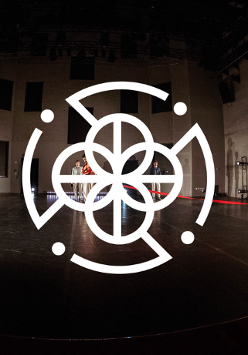 Zdjęcie sceny i czterech stojących na niej osób. Na pierwszym planie biała grafika: cztery połaczone ze sobą kółka, otoczone przerywaną obwódką.