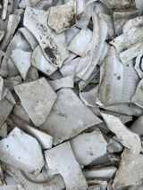 Fragmenty potłuczonych białych, brudnych naczyń; na jednym kawałku naczynia narysowana smutna buźka.