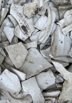 Fragmenty potłuczonych białych, brudnych naczyń; na jednym kawałku naczynia narysowana smutna buźka.