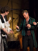 Trzech mężczyzn i jedna kobieta na scenie. Kobieta ubrana w białą suknię z wiankiem na głowie trzyma w dłoni kieliszek, mężczyźni żywo o czymś dyskutują.