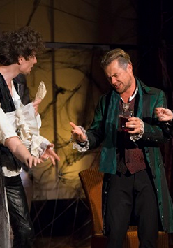 Trzech mężczyzn i jedna kobieta na scenie. Kobieta ubrana w białą suknię z wiankiem na głowie trzyma w dłoni kieliszek, mężczyźni żywo o czymś dyskutują.