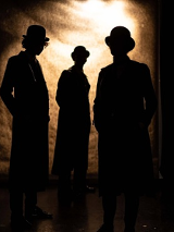 Zarys trzech postaci, za nimi jasna poświata.
