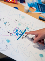 Zdjęcie pracy dziecka z dłonią wskazującą na jeden z elementów na rysunku.