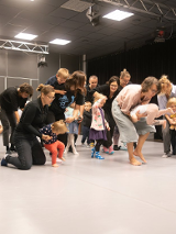 Dorośli i dzieci w ruchu w jasno oświetlonym pomieszczeniu.