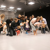 Dorośli i dzieci w ruchu w jasno oświetlonym pomieszczeniu.