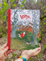 Zdjęcie ksiązki pod tyułem "Lotta. Trzy opowiadania" trzymana w dłoniach. W tle zieleniące się krzewy.