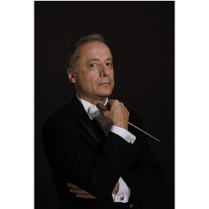 zdjęcie dyrygenta na czarnym tle, ma białą koszulę i czarna marynarkę, w ręce trzyma batutę