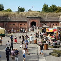 Ludzie chodzący po terenir fortu pomiędzy budkami z jedzeniem, straganami i innymi atrakacjami.
