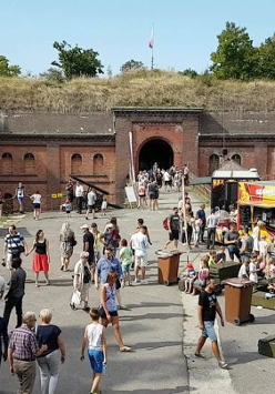 Ludzie chodzący po terenir fortu pomiędzy budkami z jedzeniem, straganami i innymi atrakacjami.