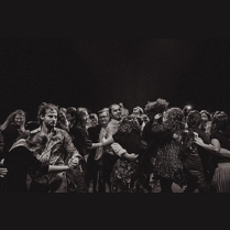 Czarno-biała fotografia z zamkowej Potańcówki. Zbliżenie na roześmianych, tańczących ludzi.