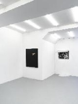 Zdjęcie z wystawy. Minimalistyczna biała przestrzeń galerii, na ścianach wiszą obrazy.