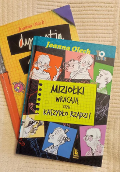 Dwie ksiązki z kolorowymi okładkami leżą na sobie po ukosie na beżowym miękkim tle.