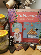 Książka, a obok miody i przed nimi pierniczki.