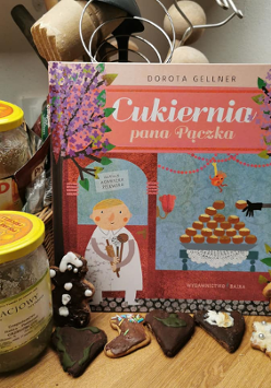 Książka, a obok miody i przed nimi pierniczki.